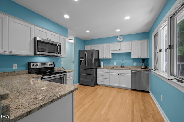 kitchen with stainless steel appliances, white cabinets, light stone counters, light wood-style flooring, and recessed lighting