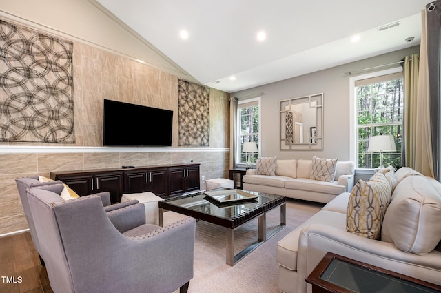 living area with lofted ceiling, recessed lighting, healthy amount of natural light, wood finished floors, and tile walls