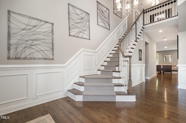 stairway featuring a decorative wall, wood finished floors, a chandelier, wainscoting, and a high ceiling