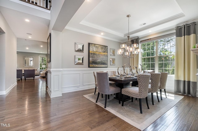 dining area featuring healthy amount of natural light, a raised ceiling, wood finished floors, a chandelier, and crown molding