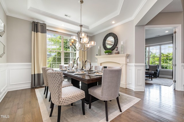 dining area featuring healthy amount of natural light, wood-type flooring, a raised ceiling, a decorative wall, and a chandelier