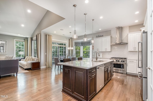 kitchen with wall chimney exhaust hood, appliances with stainless steel finishes, a sink, white cabinetry, and dark brown cabinetry