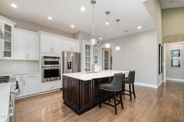kitchen featuring a sink, appliances with stainless steel finishes, light countertops, an island with sink, and white cabinetry
