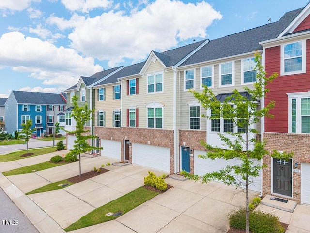 townhome / multi-family property featuring a garage, driveway, a residential view, and brick siding