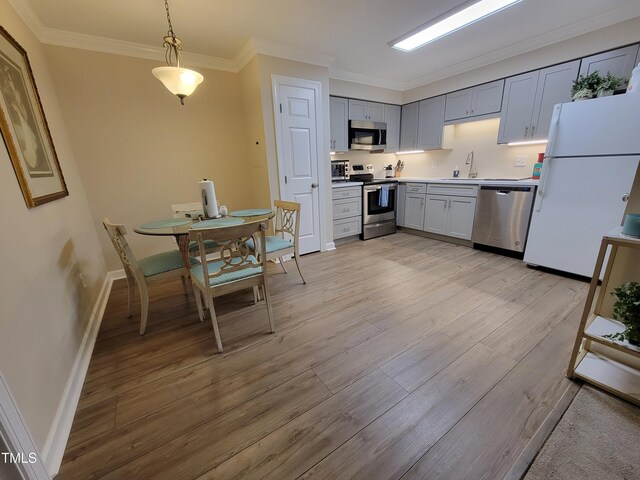 kitchen featuring appliances with stainless steel finishes, light wood-style floors, baseboards, crown molding, and light countertops