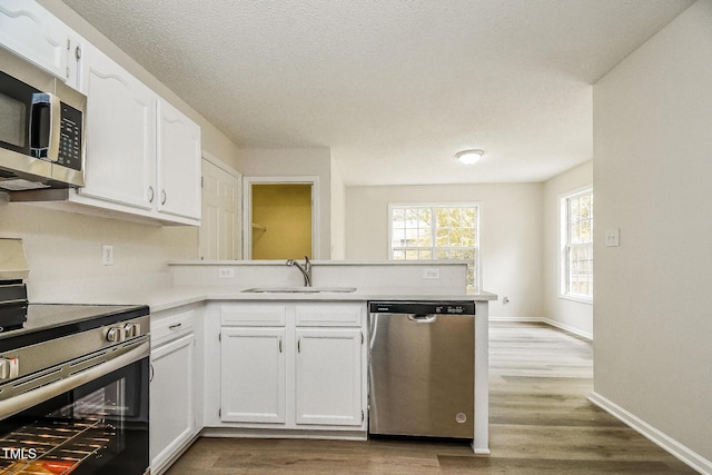 kitchen featuring stainless steel appliances, a peninsula, white cabinets, and light countertops