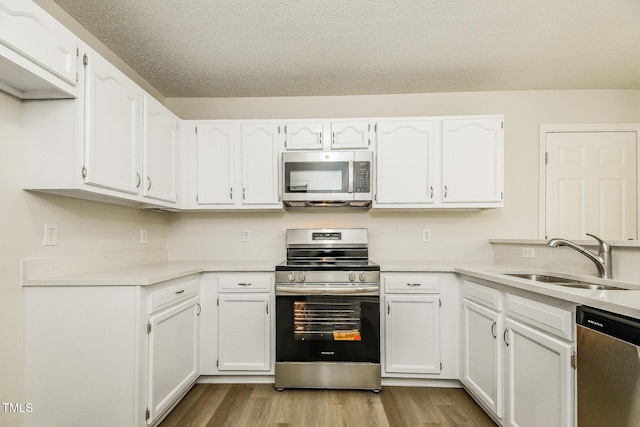 kitchen featuring stainless steel appliances, a sink, dark wood-style floors, white cabinetry, and light countertops