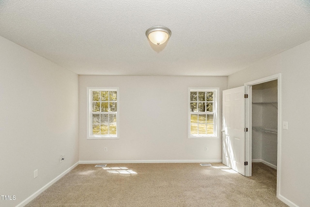 unfurnished bedroom with a spacious closet, carpet, baseboards, a textured ceiling, and a closet