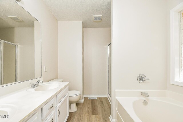 bathroom with wood finished floors, a shower stall, a bath, toilet, and double vanity