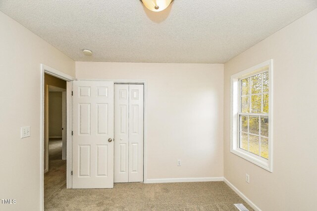 unfurnished bedroom featuring light carpet, a closet, a textured ceiling, and baseboards