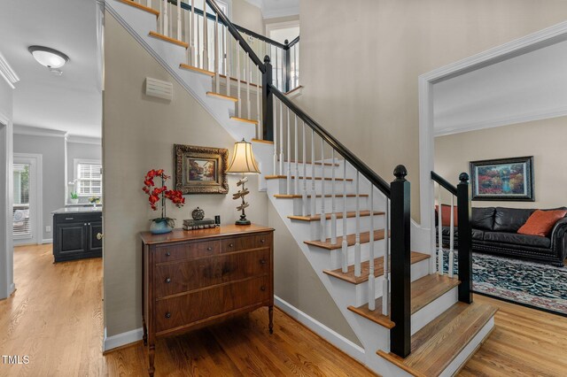 staircase with ornamental molding, wood finished floors, and baseboards