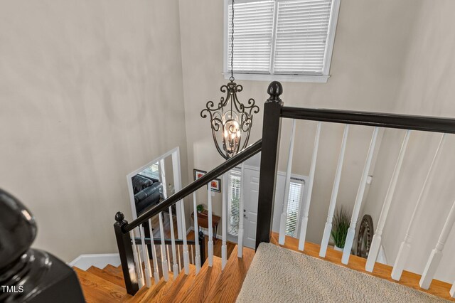 staircase with plenty of natural light, wood finished floors, a chandelier, baseboards, and a towering ceiling