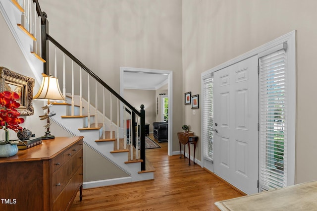 foyer with a high ceiling, wood finished floors, stairway, baseboards, and ornamental molding