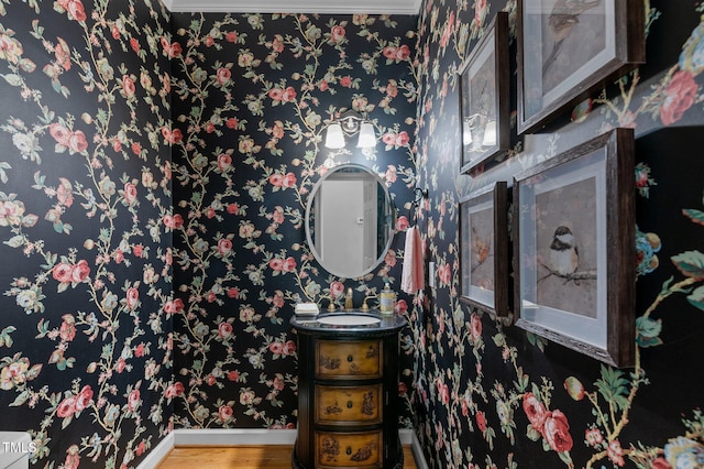 bathroom featuring wood finished floors, vanity, baseboards, and wallpapered walls