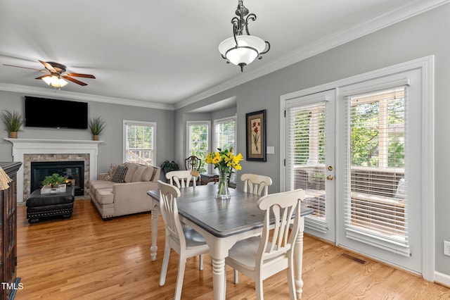 dining room featuring a ceiling fan, crown molding, light wood-style flooring, and a glass covered fireplace