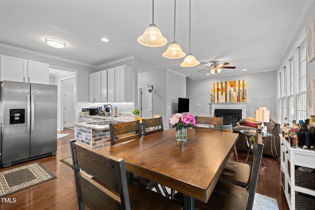 dining area featuring ceiling fan, dark wood finished floors, a glass covered fireplace, recessed lighting, and ornamental molding