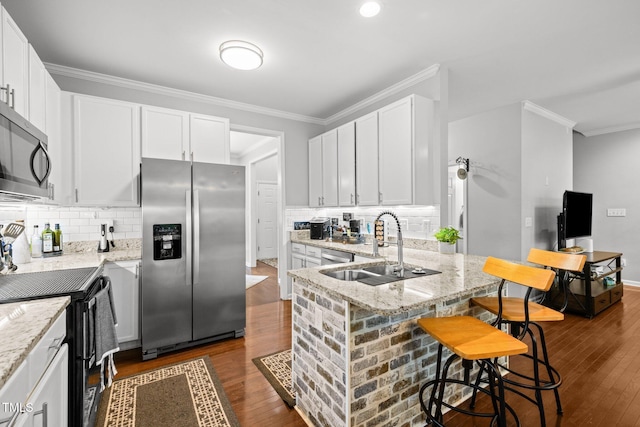 kitchen with stainless steel appliances, a sink, crown molding, dark wood-style floors, and a kitchen bar