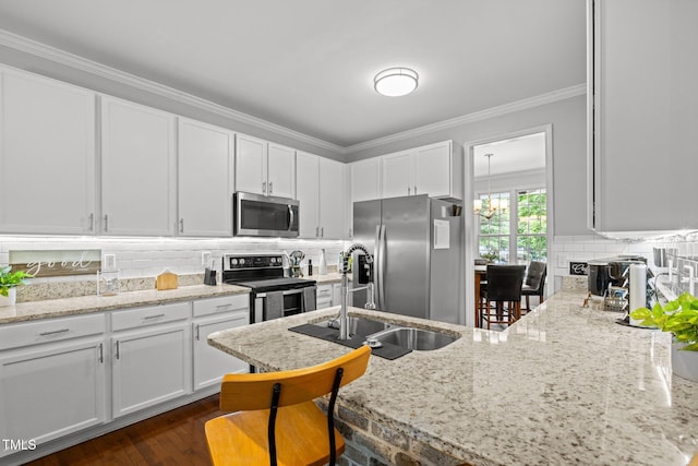 kitchen with appliances with stainless steel finishes, a sink, ornamental molding, white cabinets, and light stone counters
