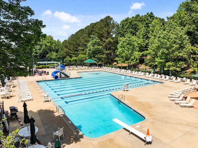 community pool with a water slide, fence, a diving board, and a patio area