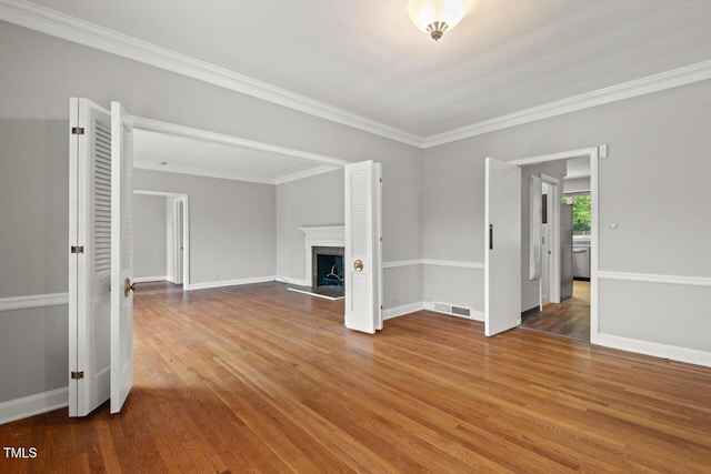 unfurnished living room featuring wood finished floors, baseboards, a fireplace, and crown molding