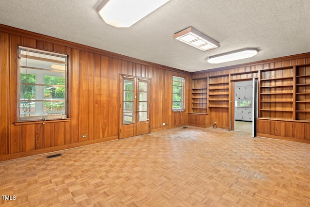 empty room featuring a textured ceiling, wood walls, baseboards, built in shelves, and ornamental molding