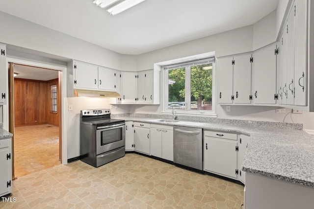 kitchen featuring appliances with stainless steel finishes, a sink, wood walls, light stone finish floors, and under cabinet range hood
