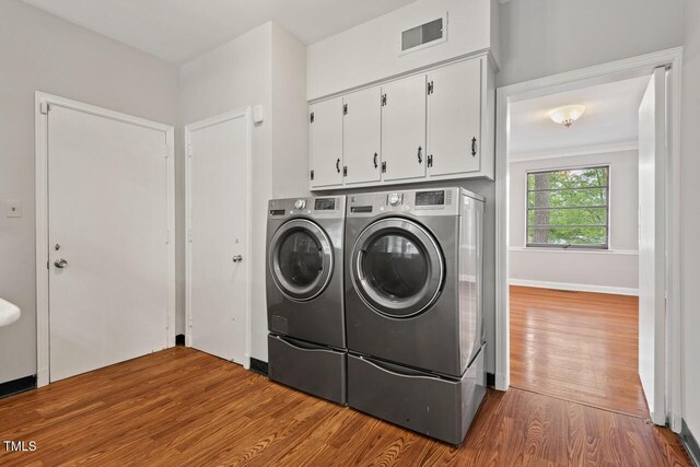 clothes washing area with cabinet space, washing machine and clothes dryer, and wood finished floors