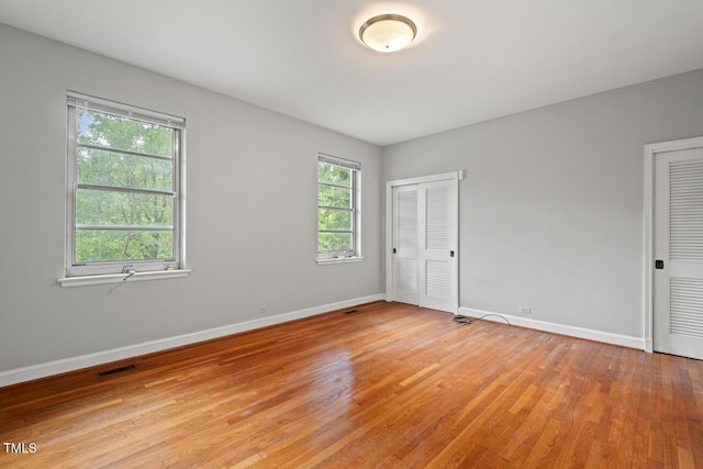 unfurnished bedroom featuring light wood-style flooring, baseboards, and multiple closets