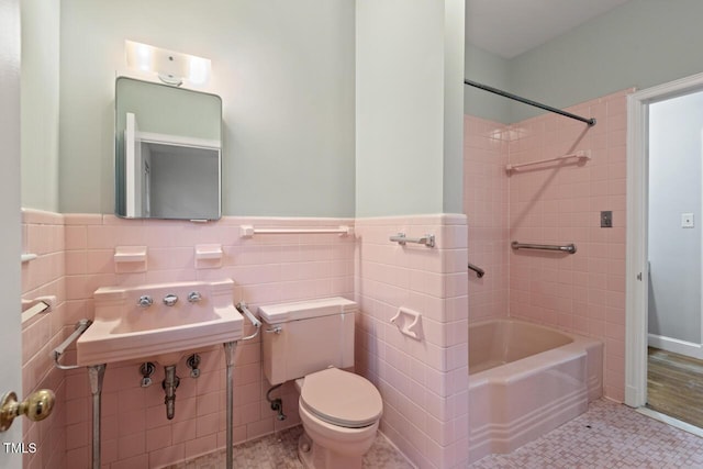 full bath with tile walls, toilet, a wainscoted wall, shower / washtub combination, and a sink