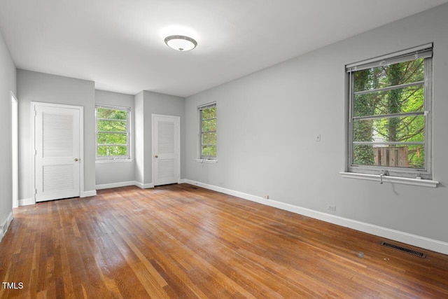 unfurnished bedroom featuring baseboards, wood finished floors, and two closets