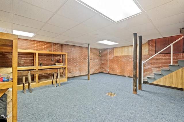 finished basement with brick wall, a paneled ceiling, carpet floors, and stairway