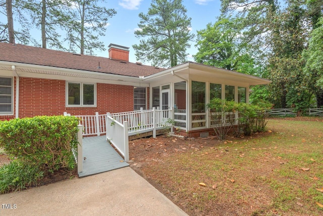 view of front of house featuring a chimney, a sunroom, a wooden deck, brick siding, and roof with shingles