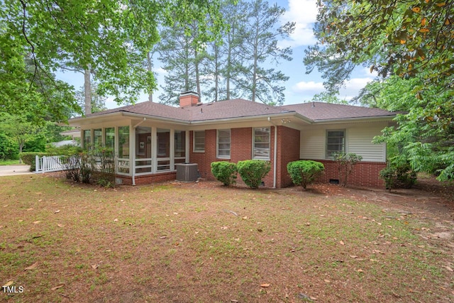rear view of house with central AC unit, a sunroom, brick siding, a lawn, and a chimney
