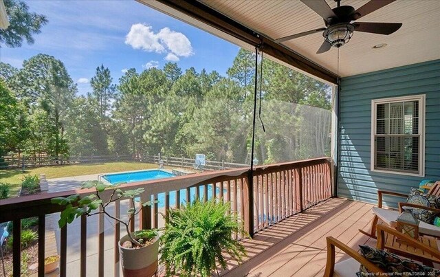wooden terrace with a ceiling fan, a fenced backyard, and an outdoor pool