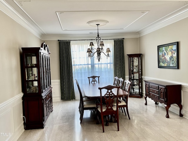 dining area featuring a chandelier, crown molding, light wood-style flooring, a decorative wall, and wainscoting