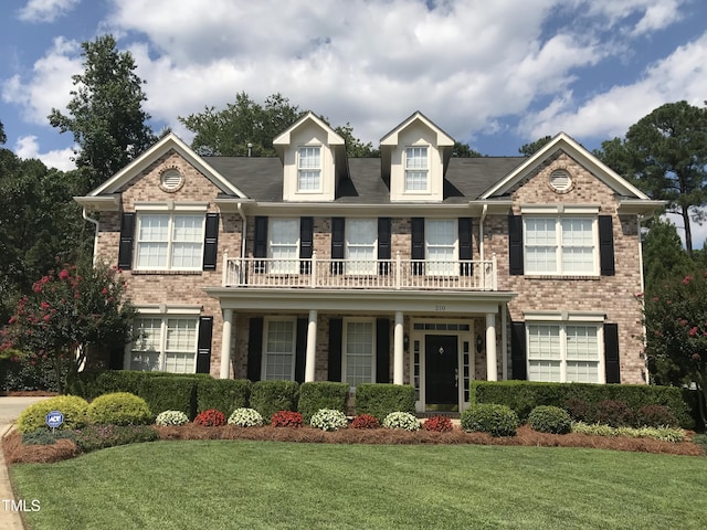 colonial house with a balcony, a front yard, brick siding, and a porch
