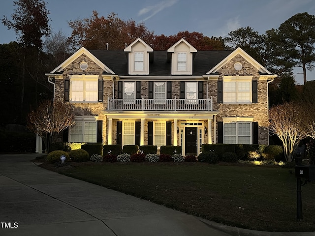 colonial inspired home featuring a balcony, a porch, and a front yard