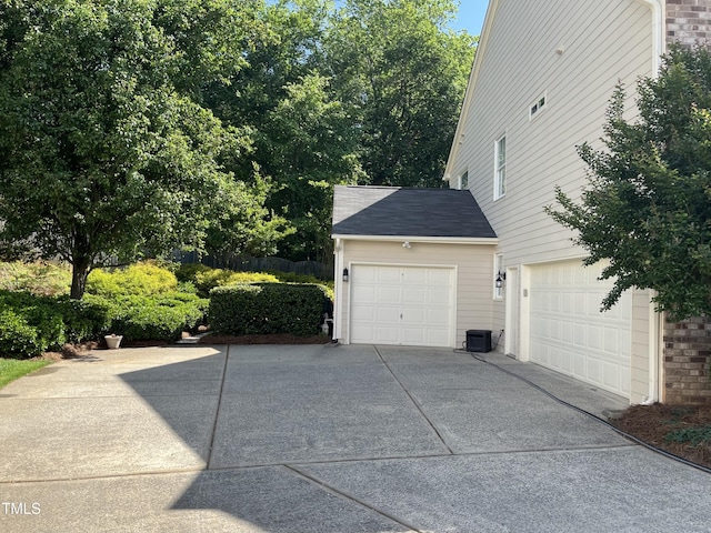 view of property exterior featuring a garage, concrete driveway, cooling unit, and a shingled roof