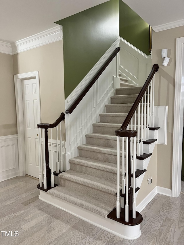stairs with crown molding, a decorative wall, a wainscoted wall, and wood finished floors