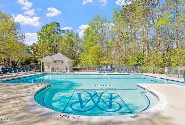 community pool with fence, a patio area, and view of wooded area