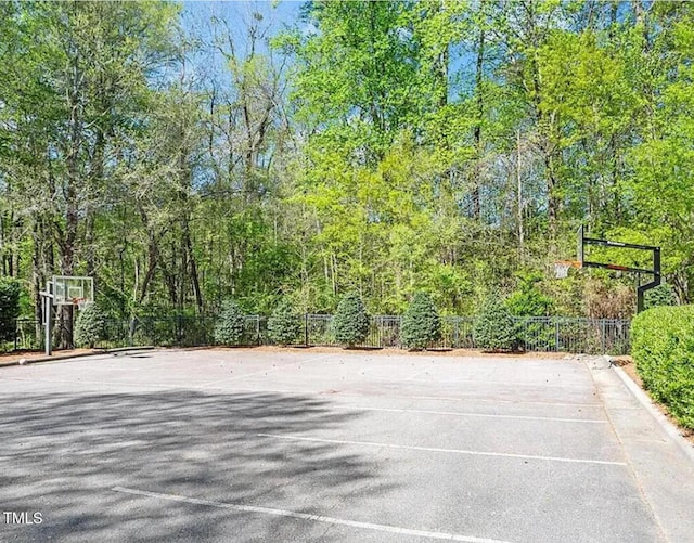 view of sport court with community basketball court, fence, and a view of trees