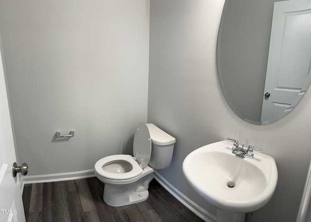 half bath with baseboards, a sink, wood finished floors, and toilet