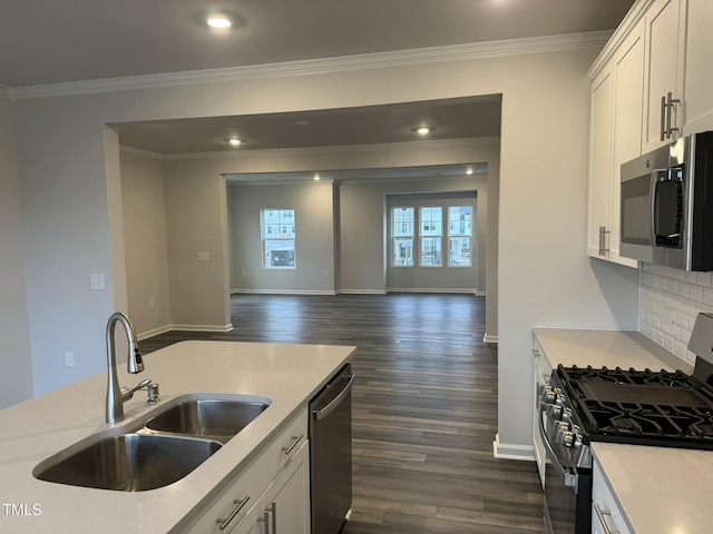 kitchen with appliances with stainless steel finishes, a sink, crown molding, dark wood finished floors, and light countertops