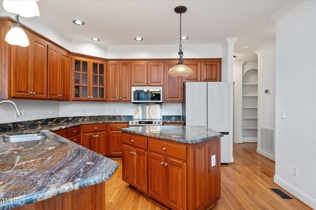 kitchen with stainless steel appliances, a sink, brown cabinetry, light wood-type flooring, and a center island