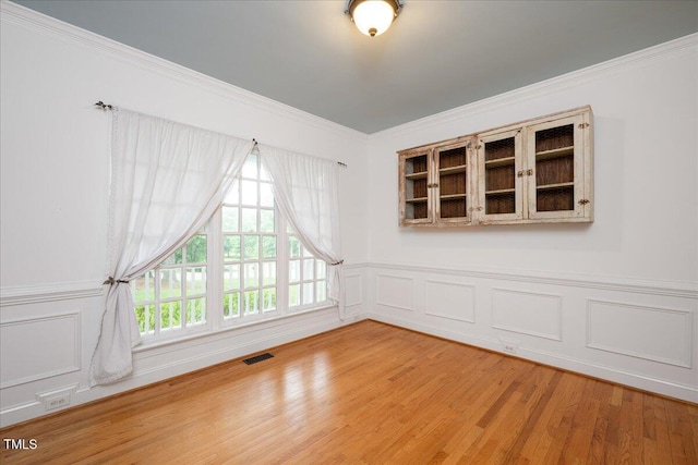 unfurnished room with wood finished floors, crown molding, a wainscoted wall, and a decorative wall