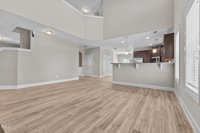 870 Kentucky Derby Ln, Lillington, NC 27546 - unfurnished living room featuring light wood-style flooring, baseboards, arched walkways, a high ceiling, and recessed lighting