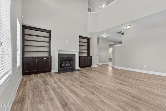 870 Kentucky Derby Ln, Lillington, NC 27546 - unfurnished living room with built in features, light wood finished floors, baseboards, a fireplace with flush hearth, and a towering ceiling