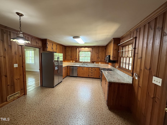 420 Rodwell St, Warrenton, NC 27589 - kitchen featuring appliances with stainless steel finishes, a sink, wooden walls, brown cabinetry, and hanging light fixtures