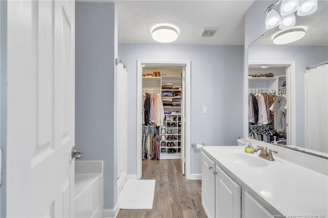 bathroom with vanity, wood finished floors, baseboards, curtained shower, and a spacious closet