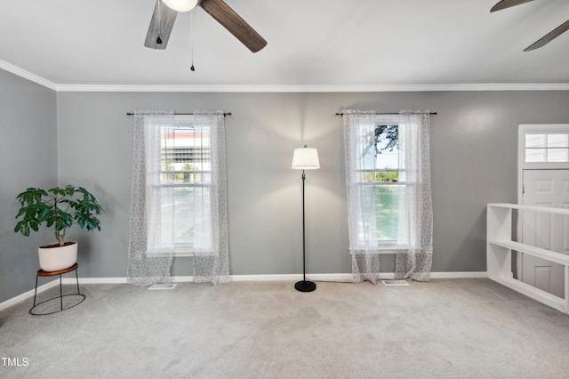 carpeted spare room with a ceiling fan, plenty of natural light, crown molding, and baseboards